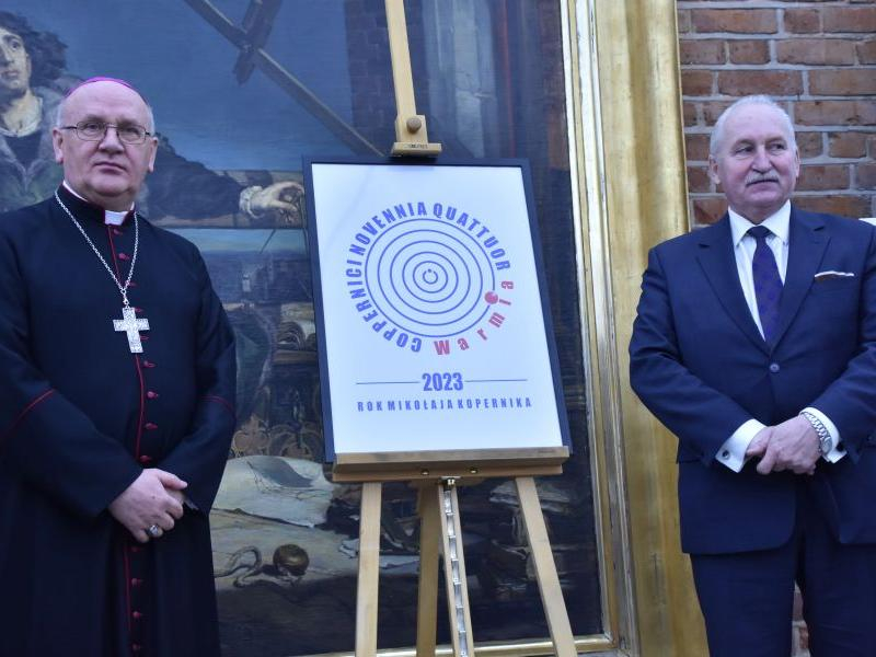 Marszałek województwa (z prawej) i arcybiskup przedstawiają logo konkursu 