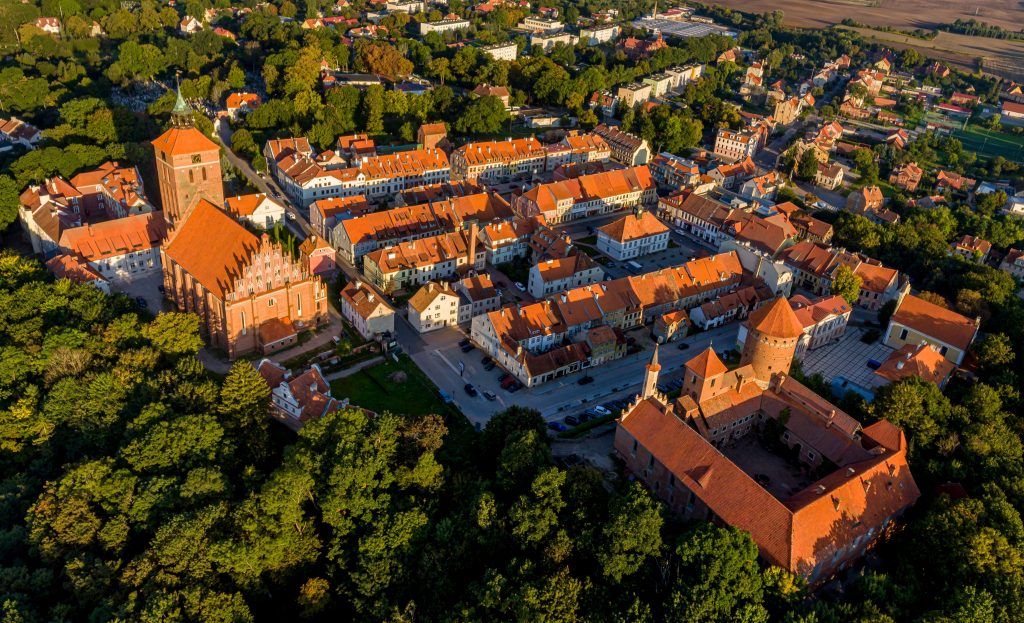 Widok z lotu ptaka na miasto z czerwonymi dachami i zielonymi drzewami.