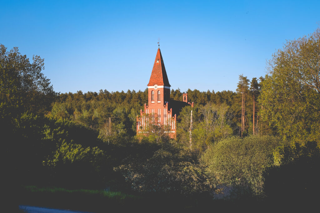 Ceglany kościół otoczony zielenią.