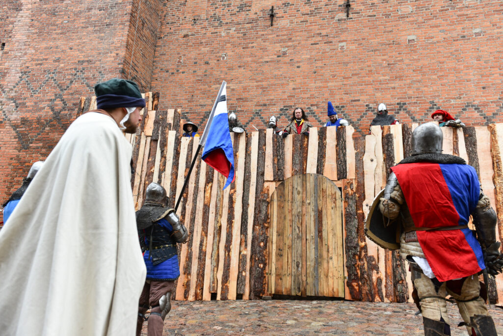 Scena z rekonstrukcji historycznej, rycerze i strażnicy na tle zamku.