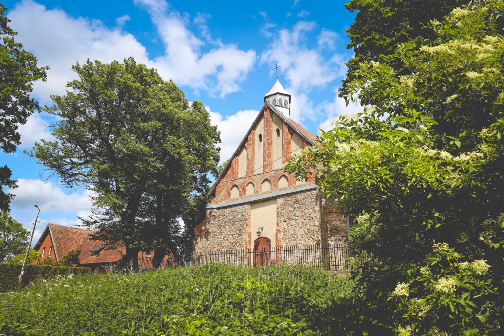 Widok kościoła otoczonego drzewami i zielenią.