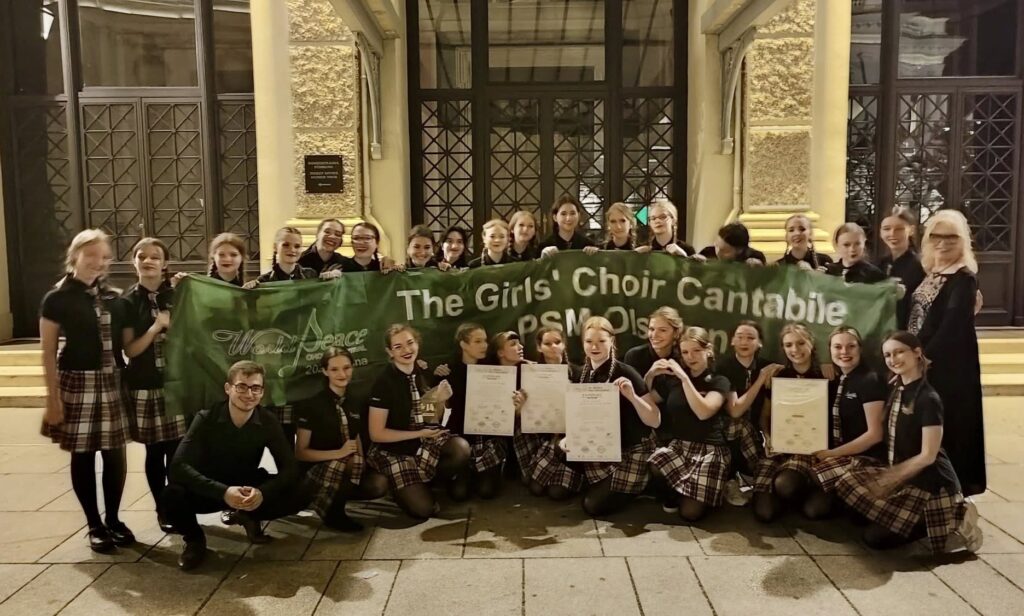 Grupa dziewcząt z chóru Cantabile z flagą i wyróżnieniami.