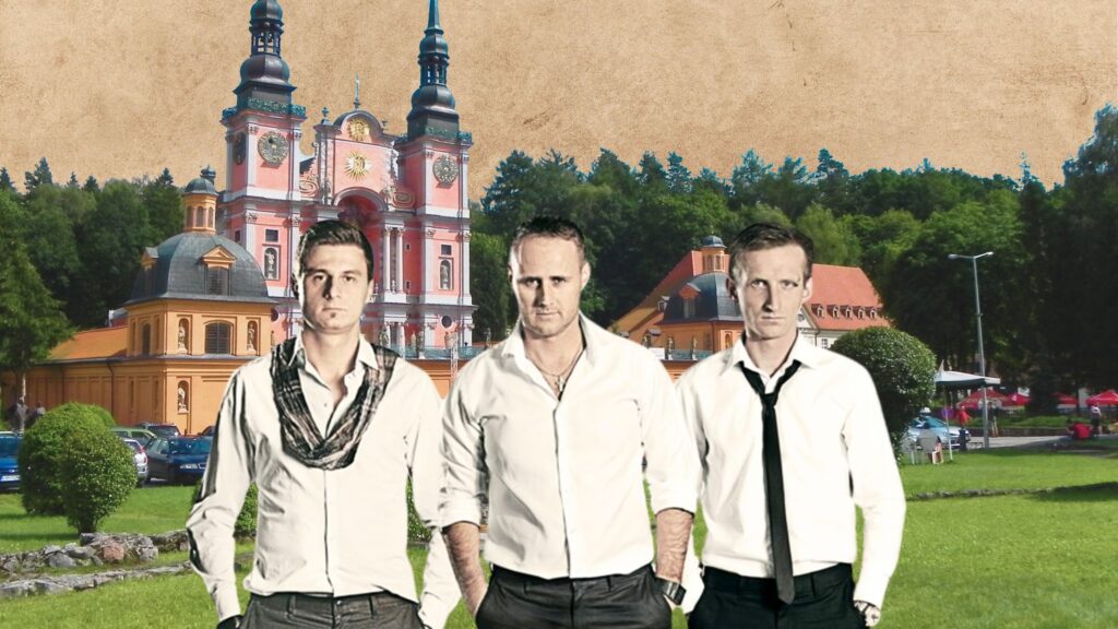 Trzech mężczyzn w białych koszulach na tle kolorowego kościoła.