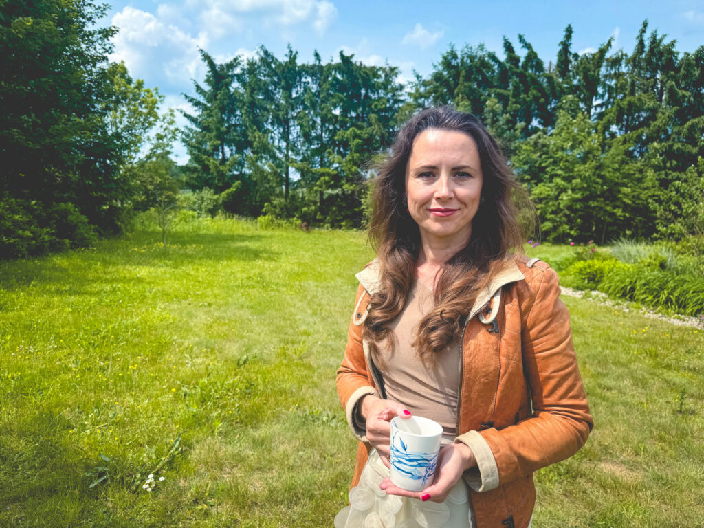 Kobieta trzymająca filiżankę na tle zielonego ogrodu.