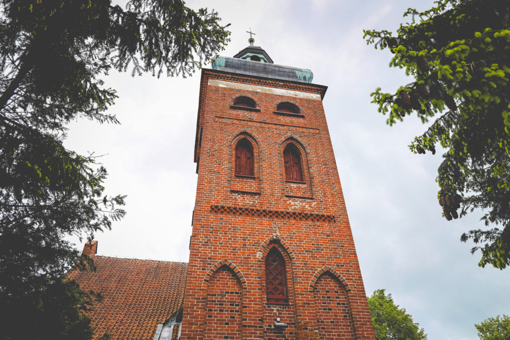 Ceglana wieża kościelna otoczona drzewami
