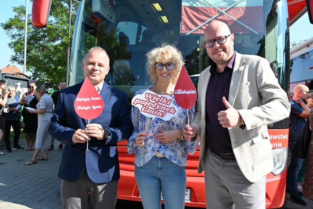 Trzej ludzie trzymają transparenty przy autobusie promującym oddawanie krwi.