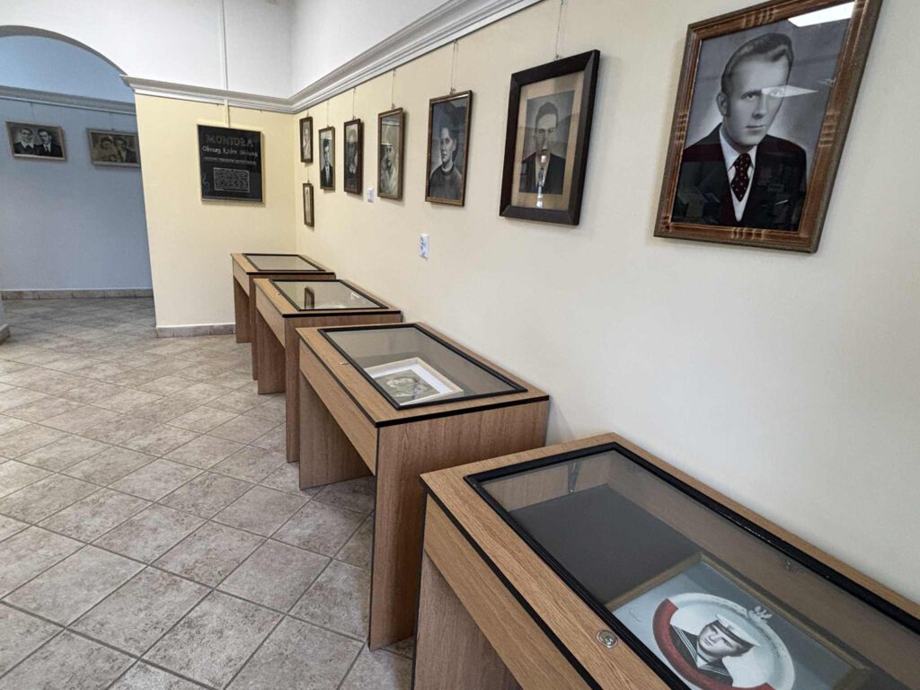 Galeria ze zdjęciami w ramkach na ścianie i wystawionymi eksponatami w szklanych gablotach.