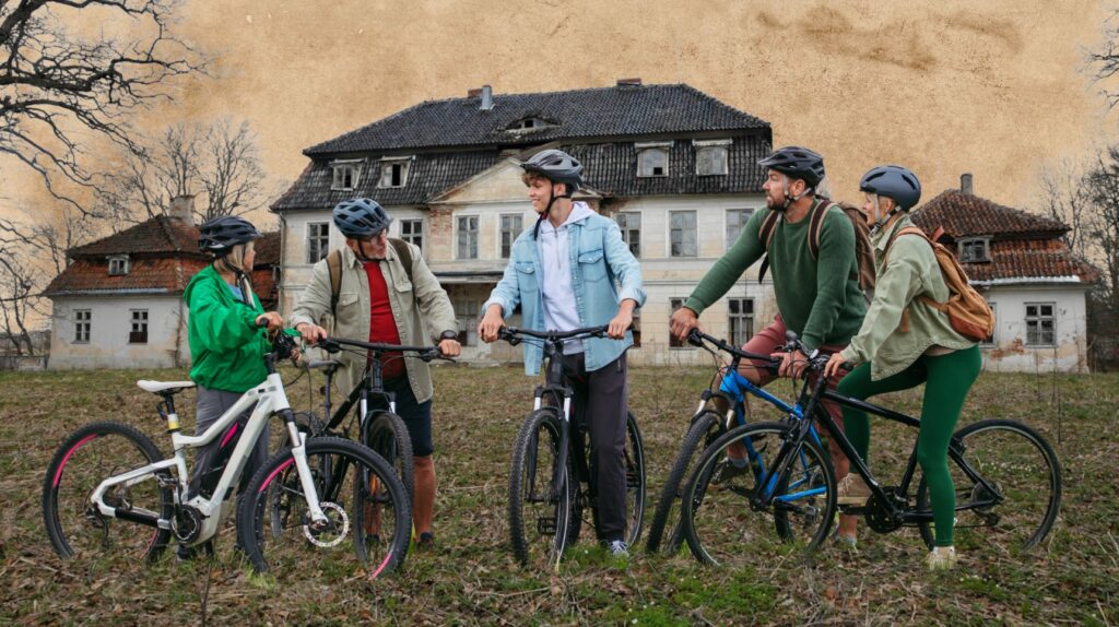 Grupa ludzi na rowerach przed opuszczonym budynkiem.