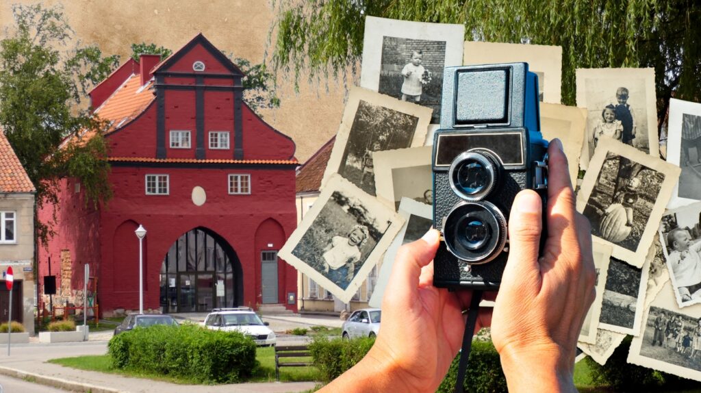 Osoba trzymająca aparat fotograficzny z dawnymi zdjęciami i czerwoną budowlą w tle.