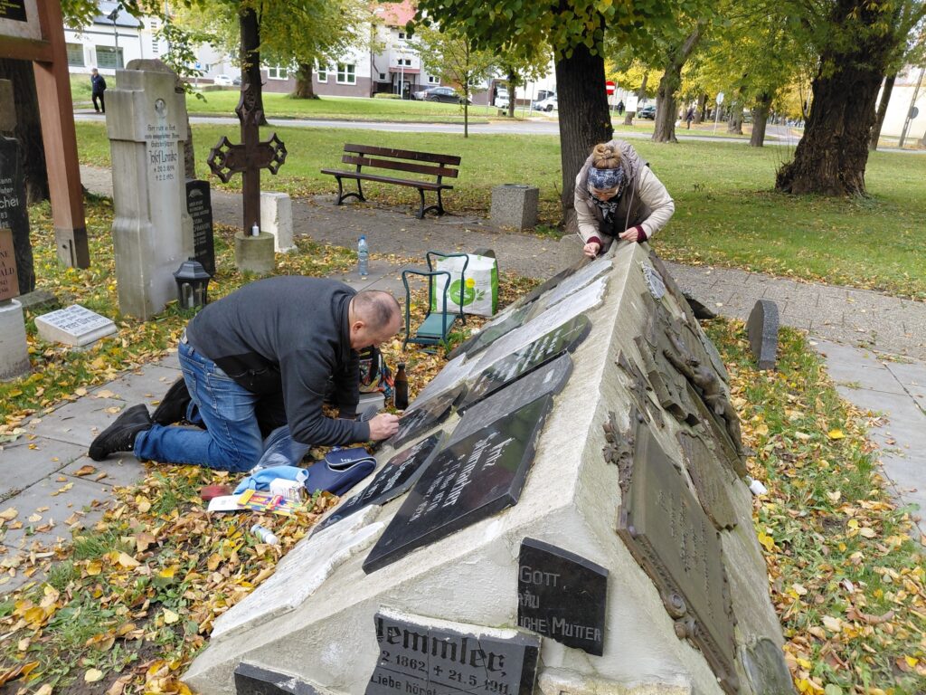 Osoby odnawiające nagrobek na cmentarzu.