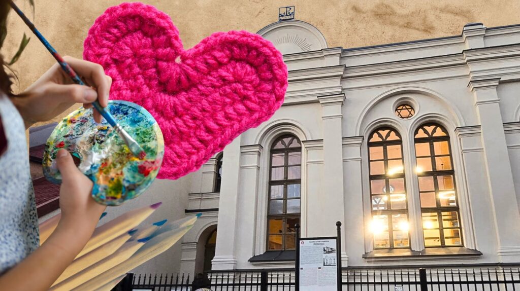 Ręka malująca z paletą i różowym sercem na tle budynku.