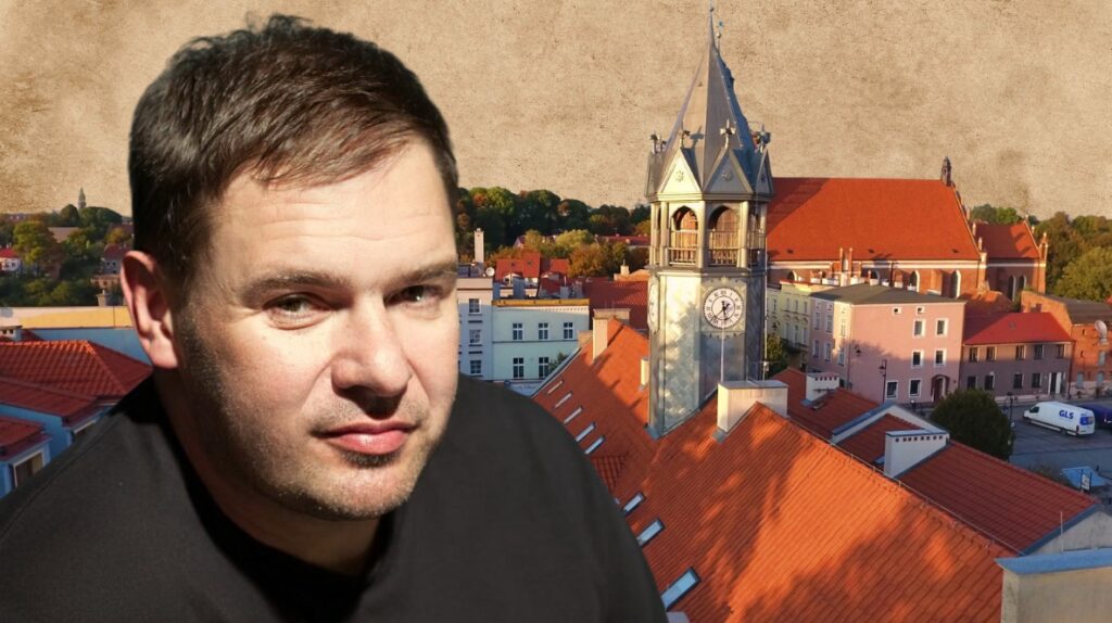 Mężczyzna na tle miasta z wieżą zegarową.