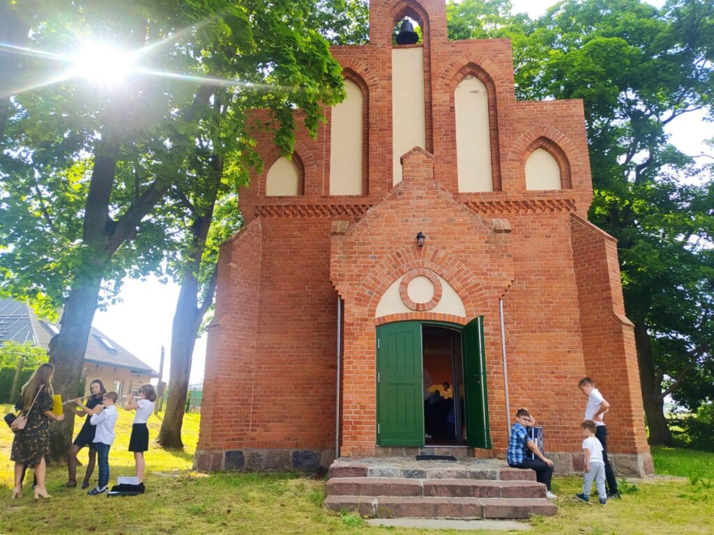 Czerwony budynek z zielonymi drzwiami i grupą ludzi na zewnątrz.