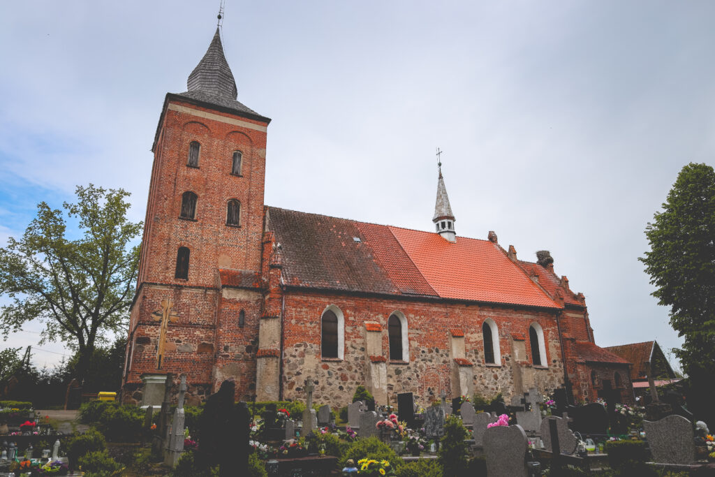 Ceglany kościół z wieżą, otoczony nagrobkami.