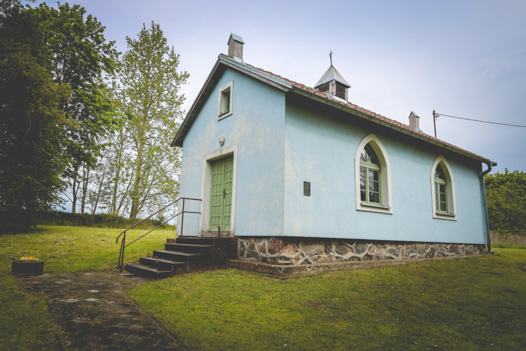 Mały, niebieski budynek sakralny z zielonymi drzwiami.