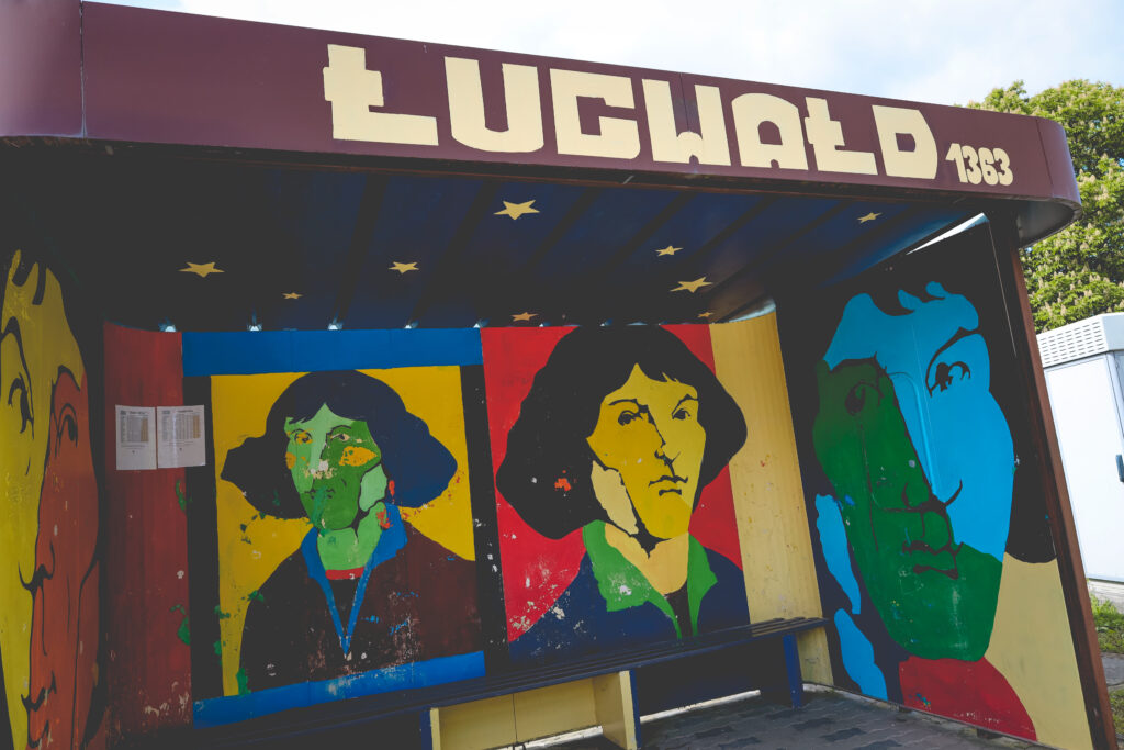 Mural na stronie przystanku autobusowego z kolorowymi twarzami.