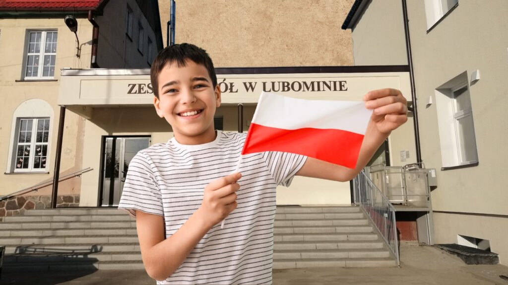 Chłopiec trzymający polską flagę przed szkołą.
