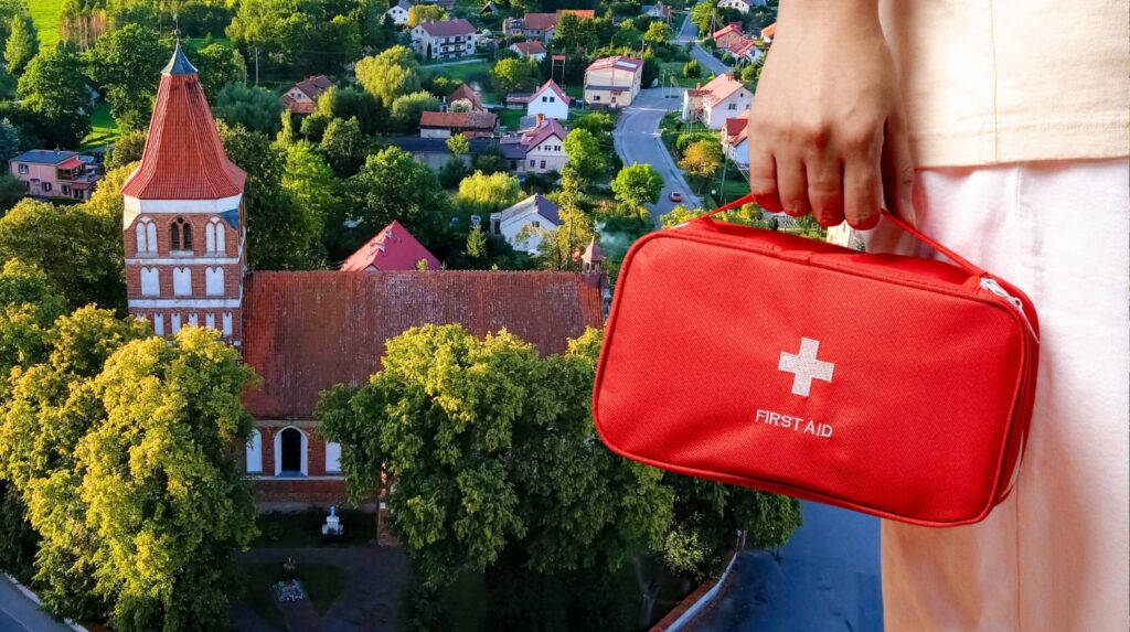 Osoba trzymająca czerwoną torbę pierwszej pomocy z widokiem na miasto.