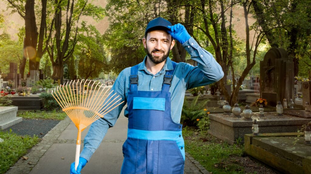 Mężczyzna z grabiami wśród grobów.