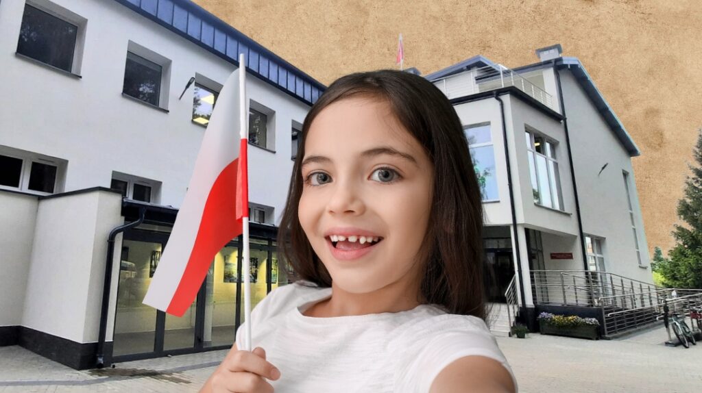 Dziewczynka trzymająca flagę Polski przed budynkiem.
