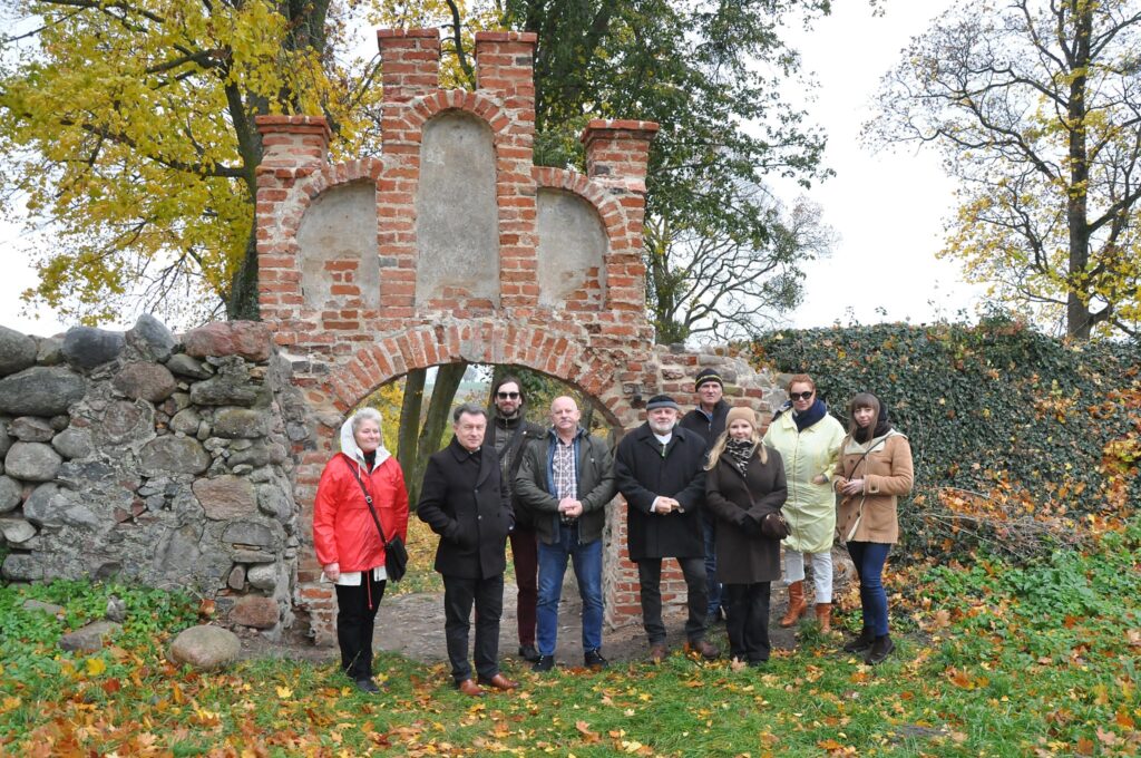 Grupa ludzi stojąca przed ruinami bramy.