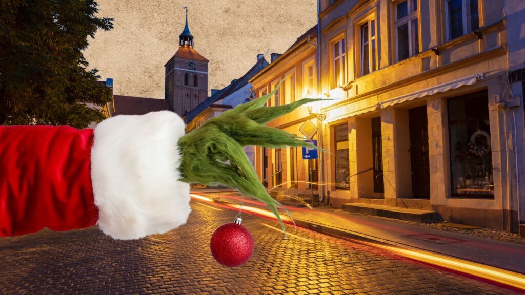 Ręka w czerwonym płaszczu trzymająca ozdobę bożonarodzeniową na tle ulicy.