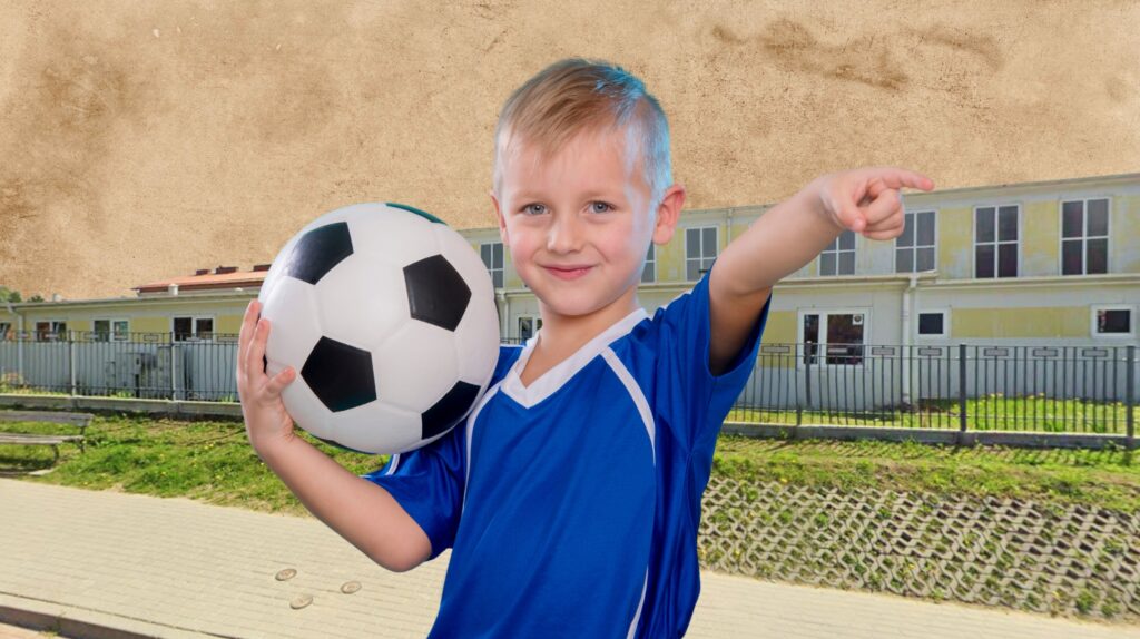 Chłopiec w niebieskiej koszulce trzyma piłkę nożną