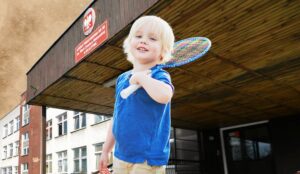 Chłopiec z rakietą przy budynku szkoły.