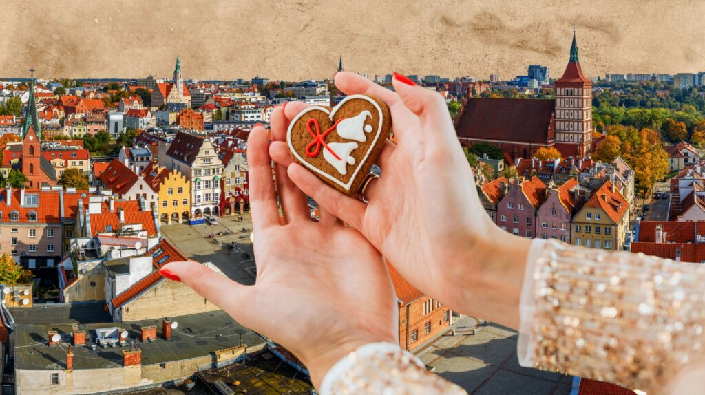 Osoba trzyma piernik w kształcie serca na tle miasta.
