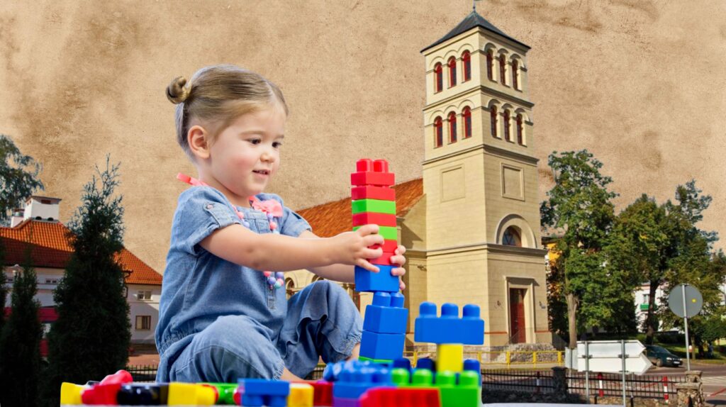 Dziecko buduje wieżę z klocków obok wieży kościoła.