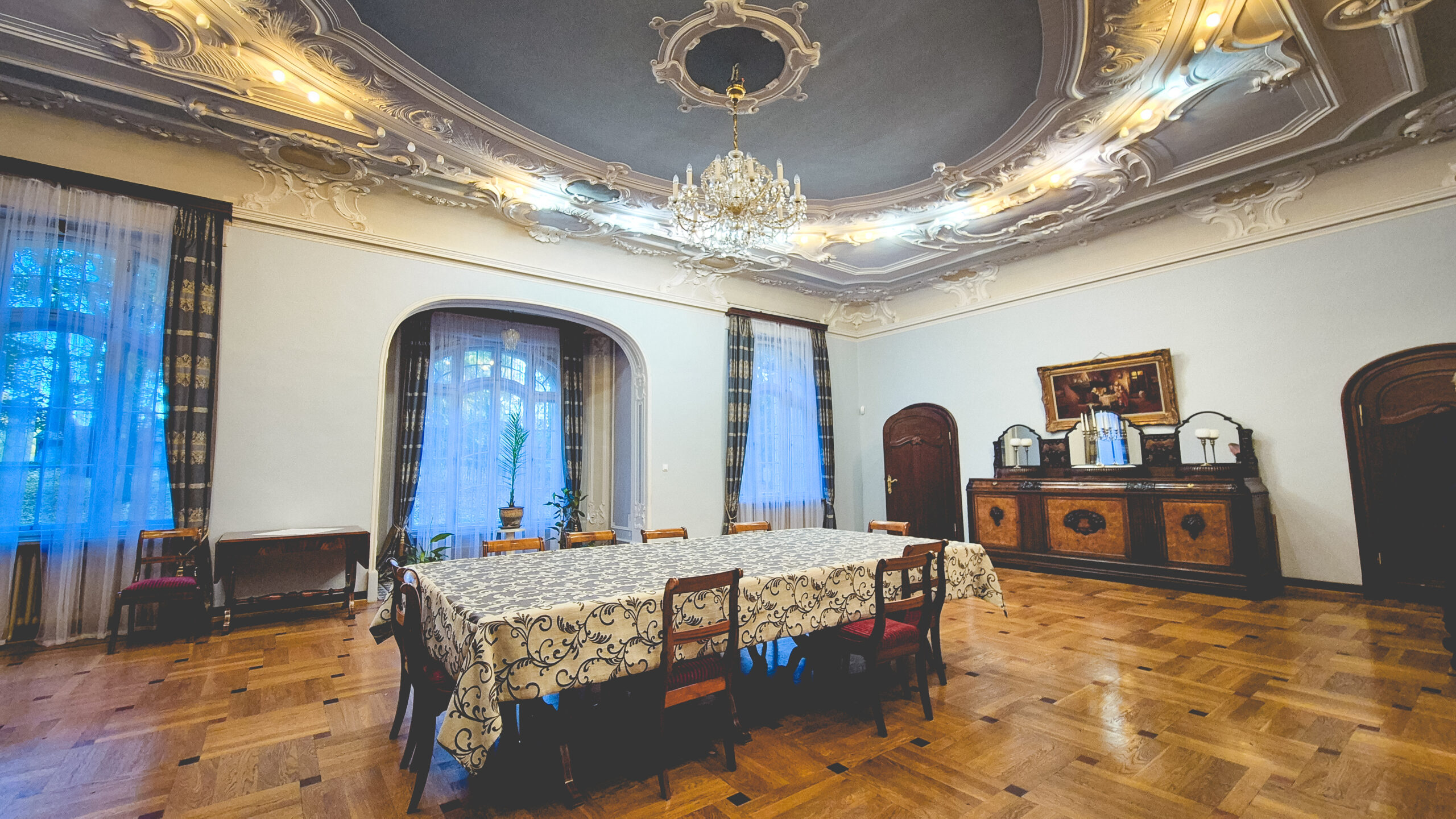 Elegancka sala z dużym stołem i ozdobnym sufitem.