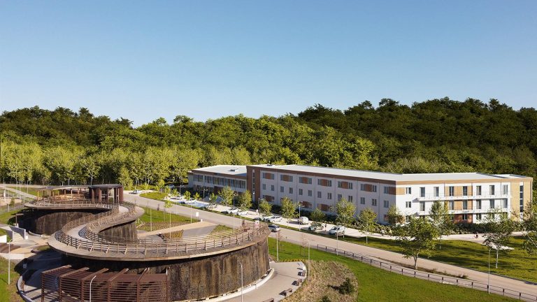 Widok nowoczesnego budynku mieszkalnego otoczonego zielenią.