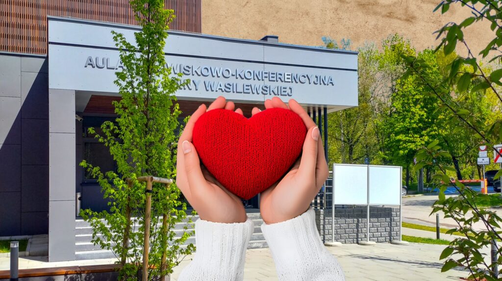 Dwie ręce trzymają czerwoną serce przed budynkiem.