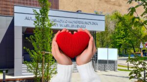 Dwie ręce trzymają czerwoną serce przed budynkiem.