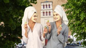 Dwie kobiety w pielęgnacyjnych maseczkach na twarzy trzymają ogórki.