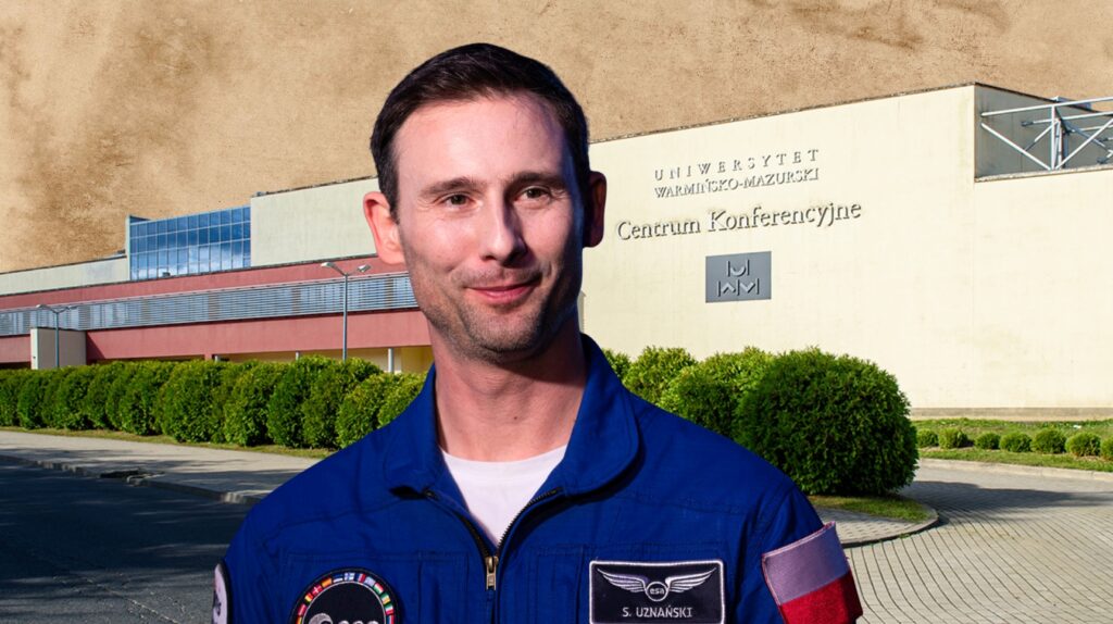 Mężczyzna w mundurze astronauty przed budynkiem konferencyjnym.