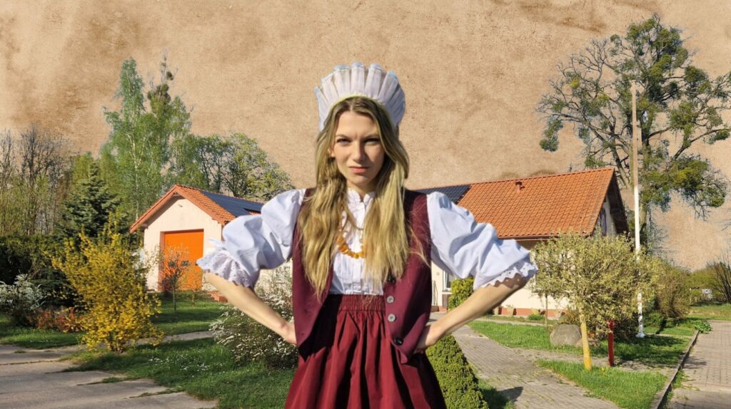 Kobieta w tradycyjnym stroju na tle wiejskiego krajobrazu.