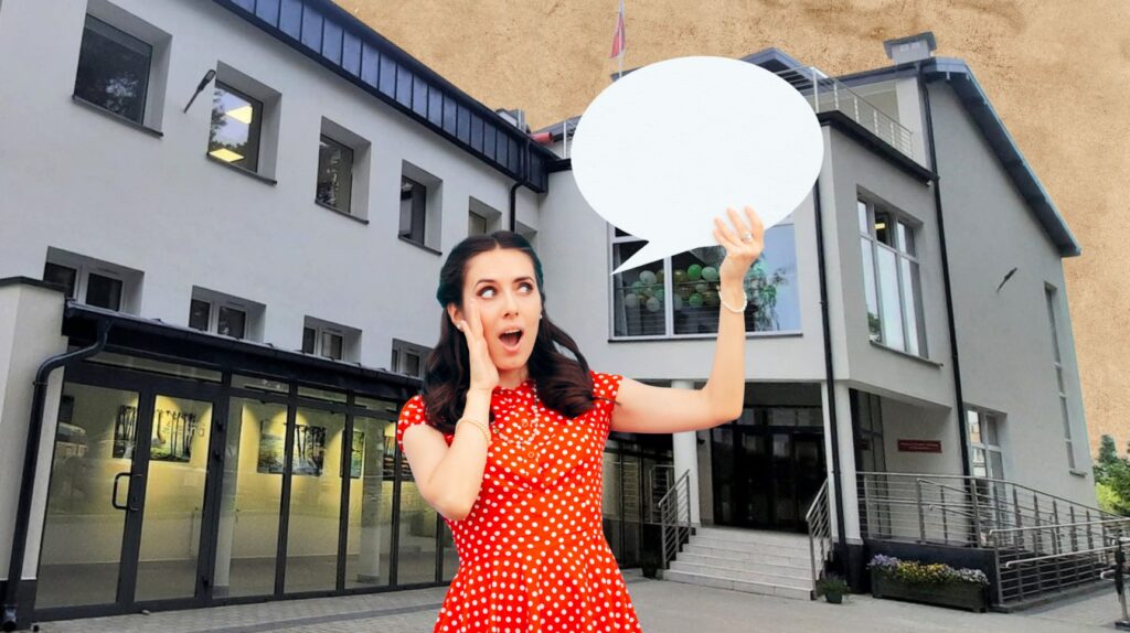 Kobieta w czerwonej sukience w grochy z wyrazem zdziwienia przed budynkiem.