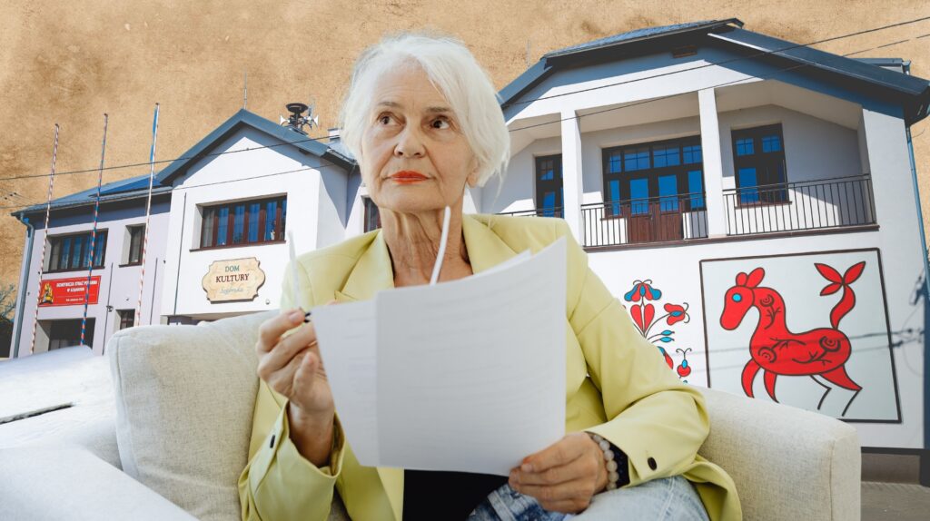 Starsza kobieta siedzi z dokumentem w ręku przed budynkiem Domu Kultury.