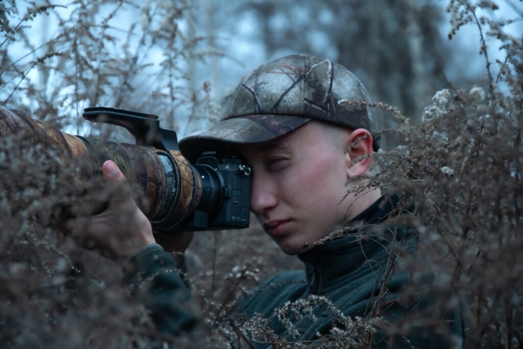 Osoba fotografująca w lesie z dużym obiektywem.