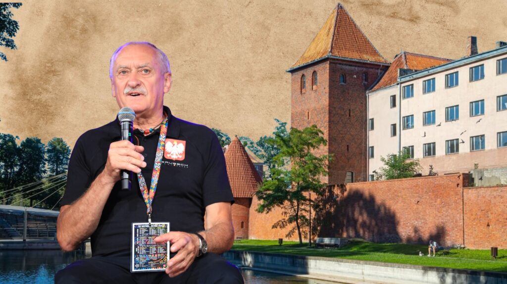 Mężczyzna z mikrofonem na tle budynków.