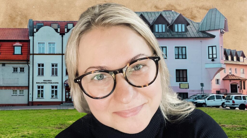 Kobieta w okularach z miejską biblioteką w tle.