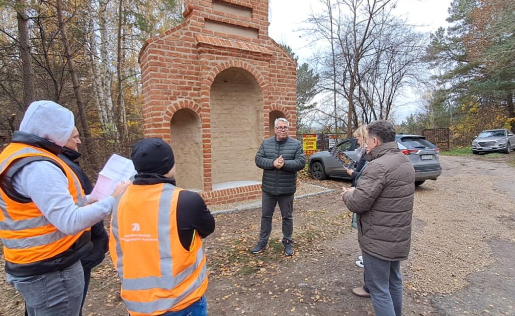 Grupa ludzi omawia budowlę przy drodze.