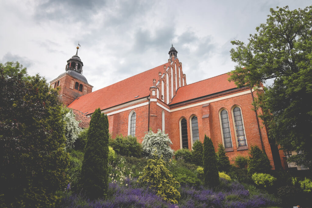 Widok na ceglany kościół otoczony roślinnością.