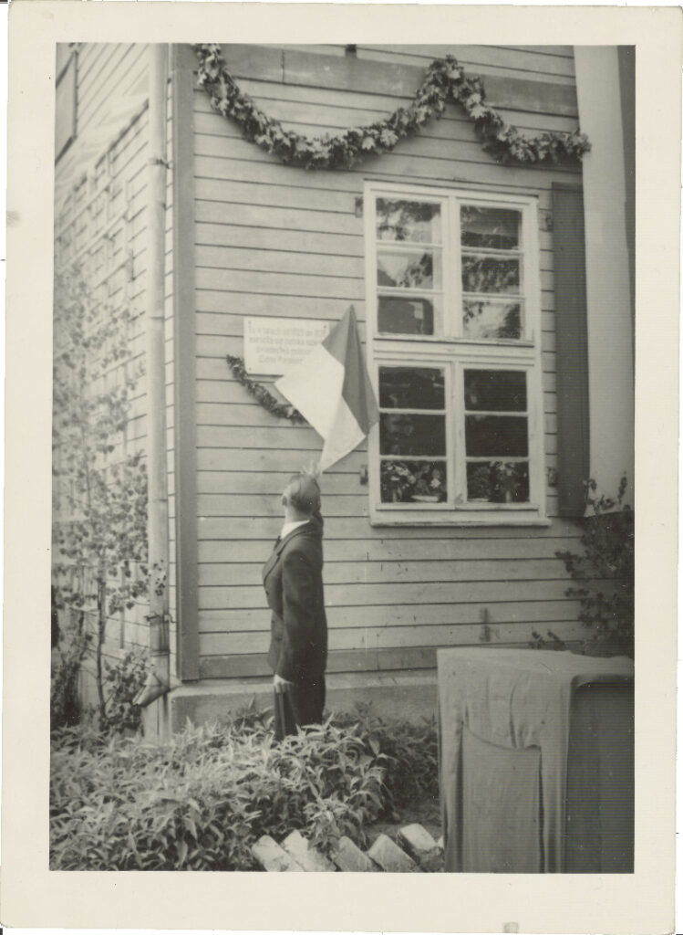 Osoba w stroju wojskowym przy murze z flagą.