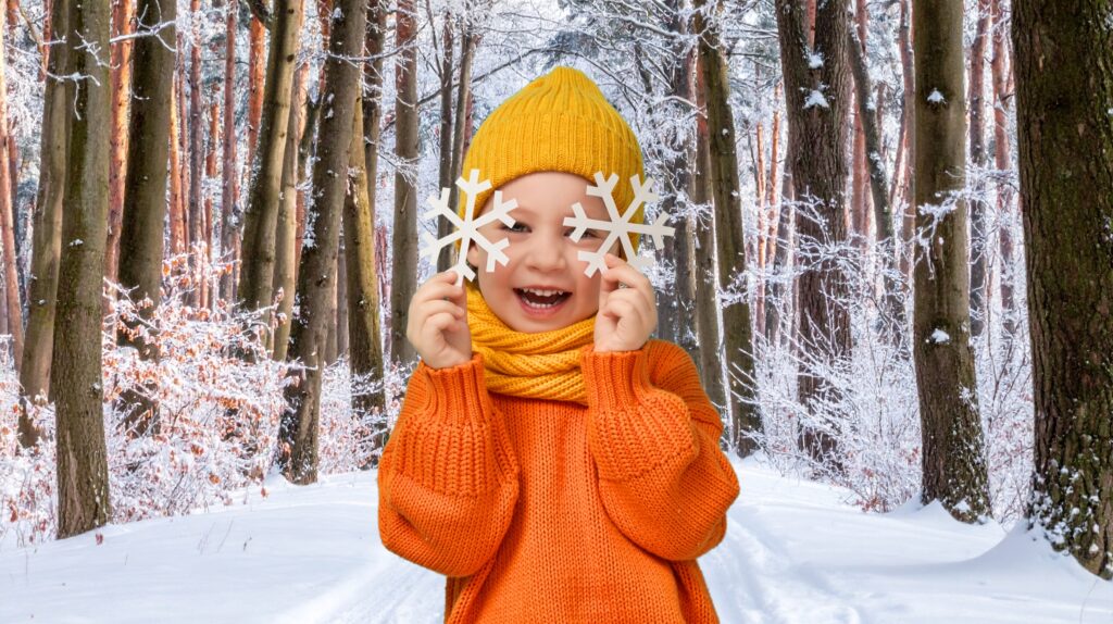 Uśmiechnięte dziecko trzymające papierowe płatki śniegu w lesie zimowym.