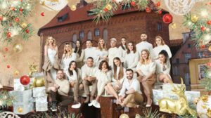 Grupa ludzi w świątecznych swetrach pozująca przed budynkiem.