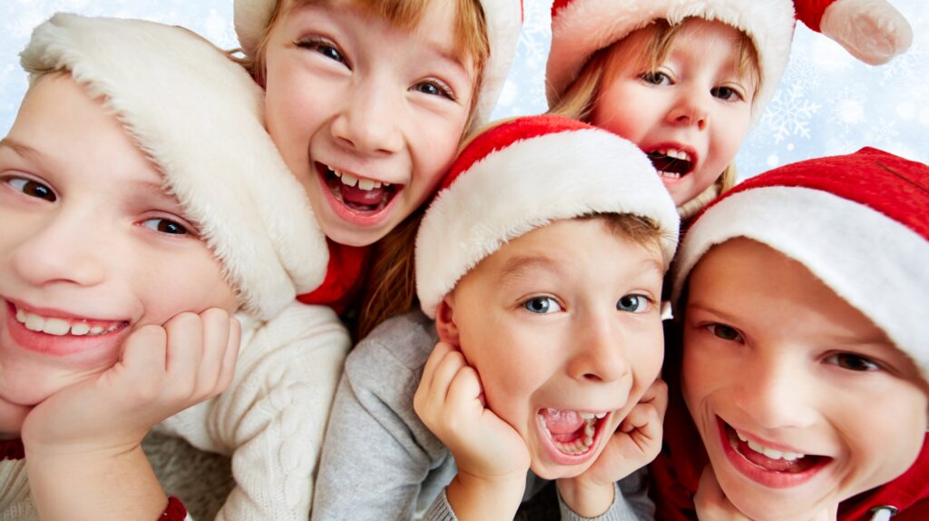 Grupa dzieci w czapkach świątecznych uśmiecha się radośnie.