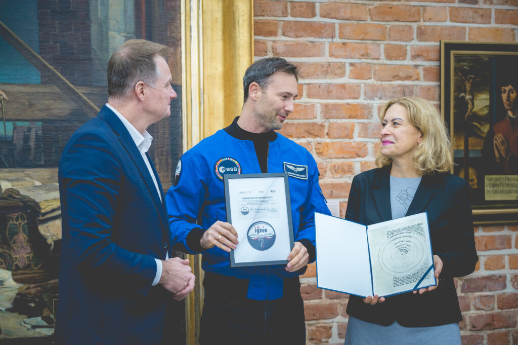 Trzech ludzi prezentuje certyfikaty w historycznym wnętrzu.