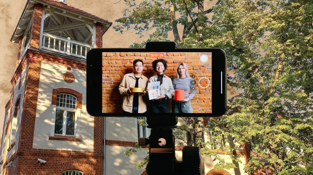 Trzy osoby pozują z kolorowymi przedmiotami przed ceglanym tłem.